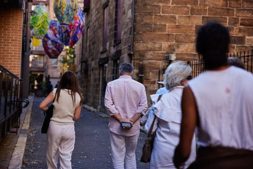 A narrow street with brick buildings, a man in a pink shirt, and colorful decorations. 2