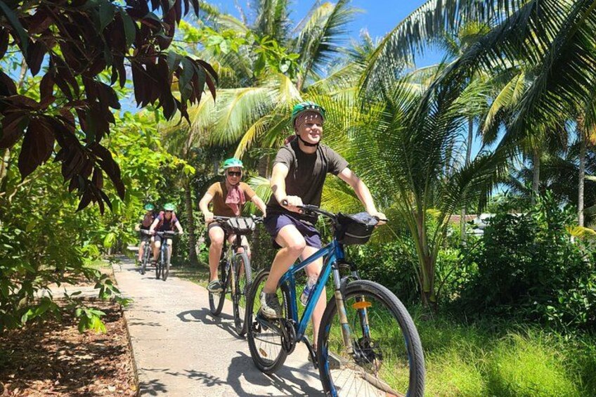 Three cyclists on a paved path surrounded by lush greenery and palm trees. 3