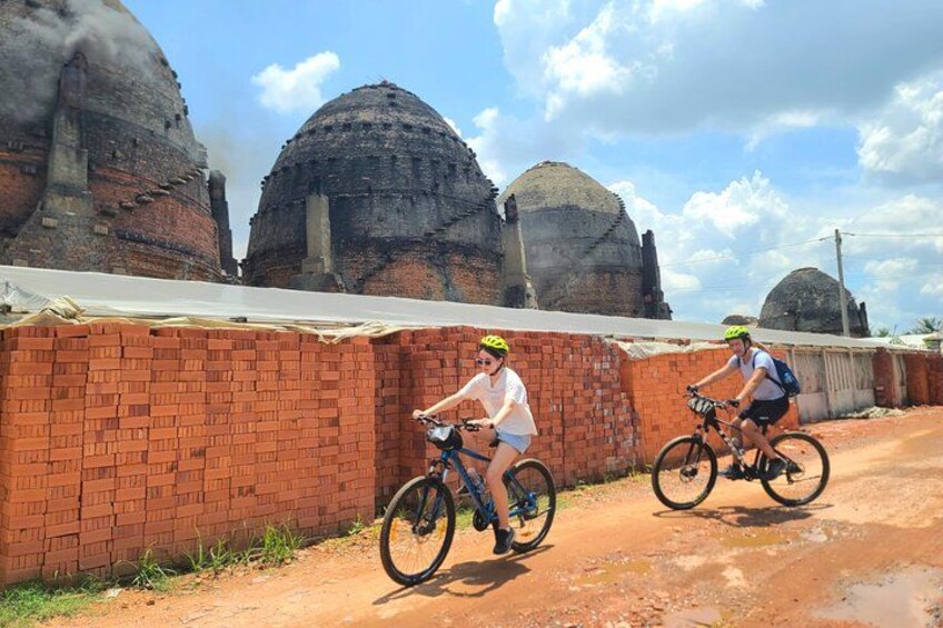 Two cyclists on a dirt path with brick walls and domed structures in the background. 3