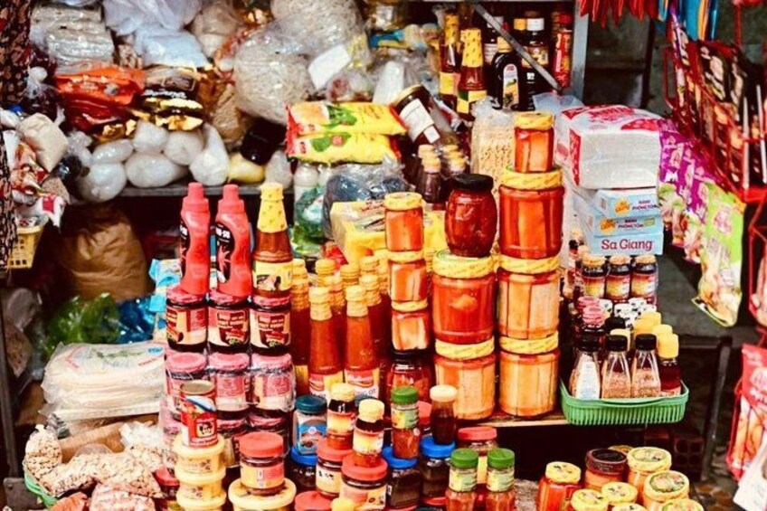Un étal de marché proposant divers produits alimentaires, notamment des pots de sauces, des bouteilles de condiments et des produits emballés. 3