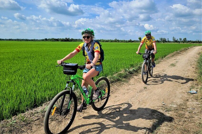 Two cyclists on a dirt path in a green field. 1
