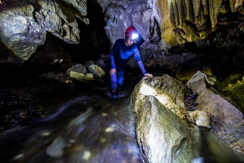 Eine Person in blauem Anzug und Helm erkundet eine Höhle mit Stalaktiten und einem Wasserlauf. 3