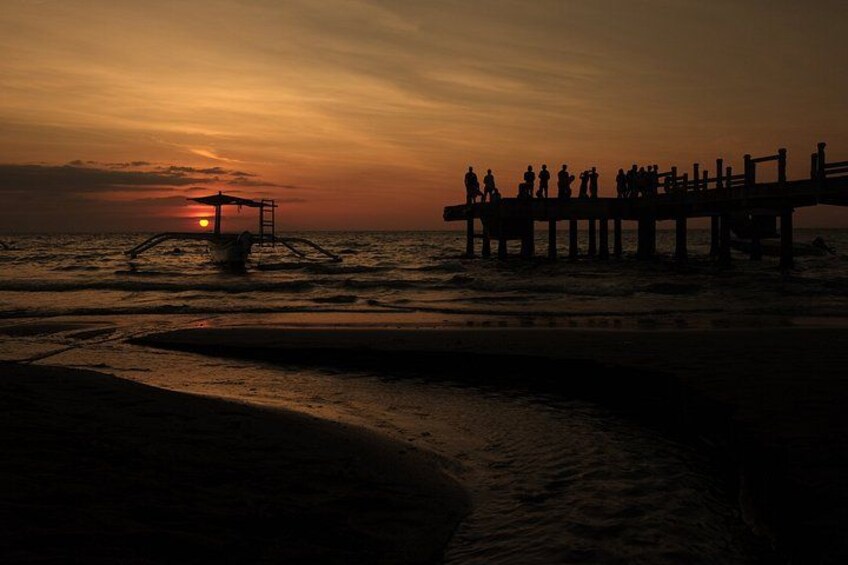 A sunset over a beach with a pier and people standing on it. 2
