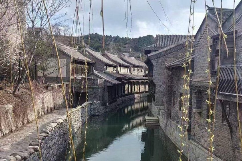 A narrow waterway flanked by traditional buildings with tiled roofs, a stone wall, and a clear sky. 5