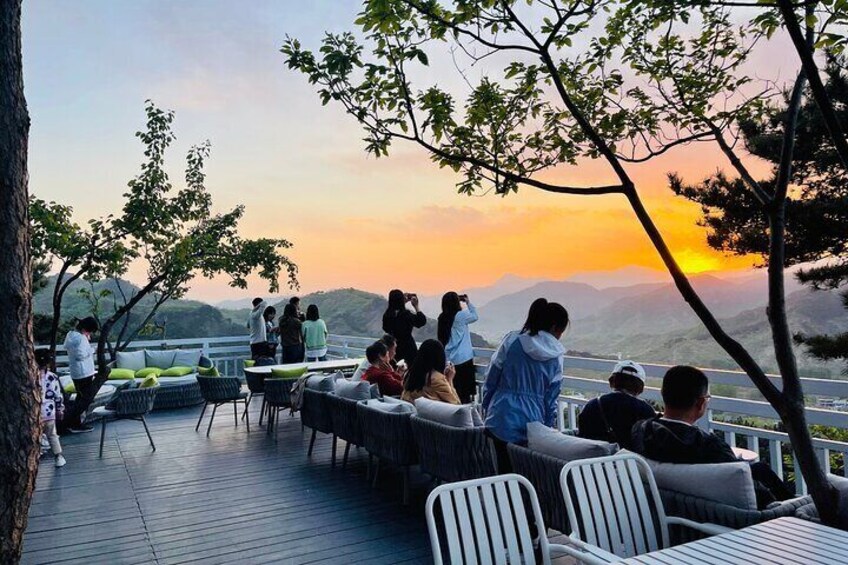 A sunset view from a terrace with people sitting and standing, overlooking a valley. 1