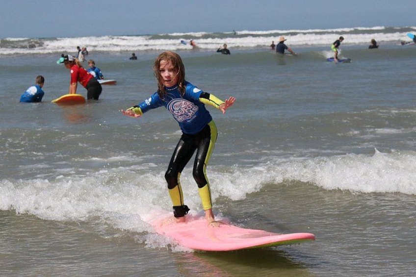 Een kind surft op een roze plank, met andere surfers op de achtergrond. 3