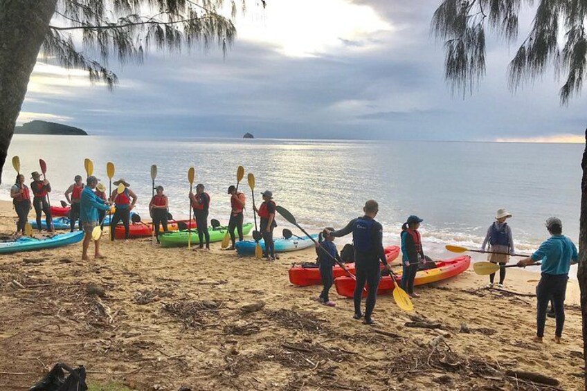 Un grupo de personas en una playa con kayaks y remos, preparándose para hacer kayak. 3