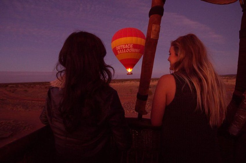 Two people watching a hot air balloon with 'OUTBACK BAILLOOING' written on it. 2
