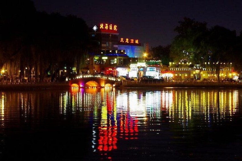 Een nachtelijke scène met een fel verlichte brug die in het water weerspiegelt, verlichte gebouwen en een rivier. 2