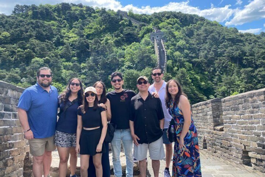 Un grupo de personas de pie sobre un muro de piedra, con una colina boscosa al fondo. 3