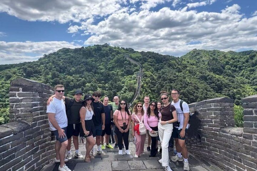 Un grupo de personas de pie sobre un muro de piedra, con una montaña boscosa al fondo. 4
