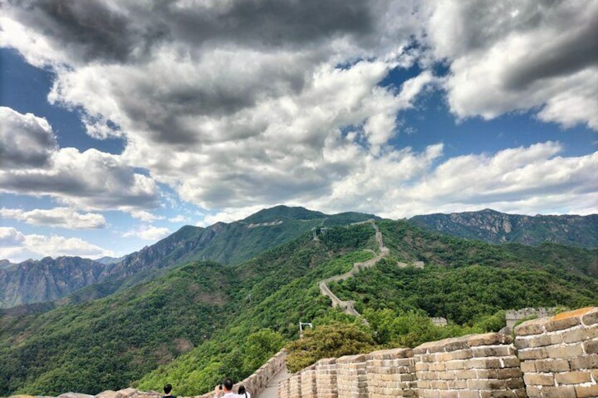A mountainous landscape with a winding path, a stone wall, and a clear sky with clouds. 3
