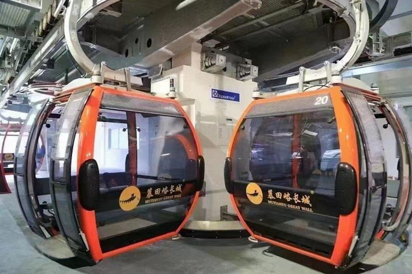 A pair of orange and black cable cars with 'MUTIANTY GREAT WALL' written on them, suspended by a cable system. 5
