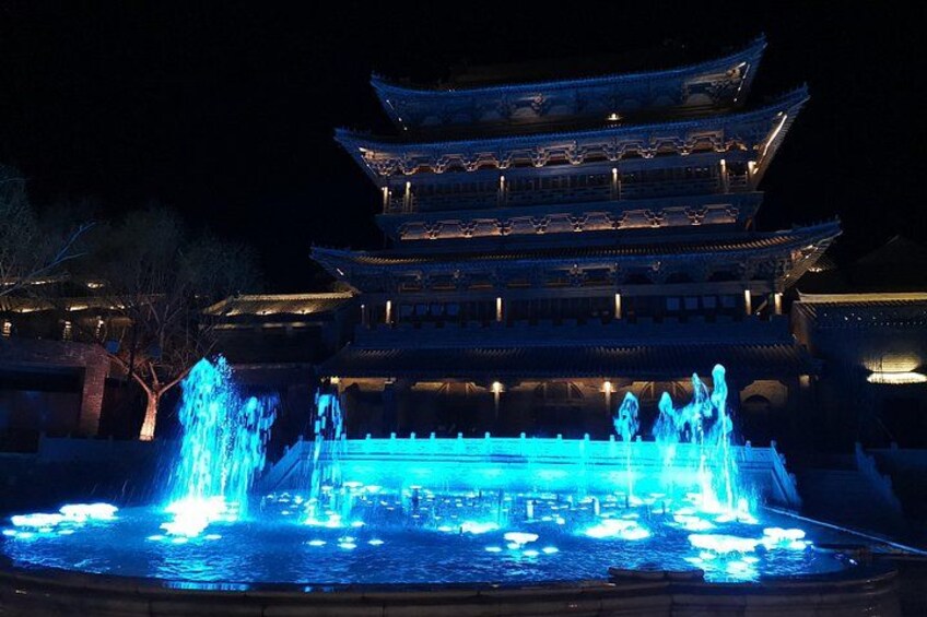 Un bâtiment traditionnel à plusieurs niveaux, illuminé de lumières bleues, avec une fontaine devant. 4
