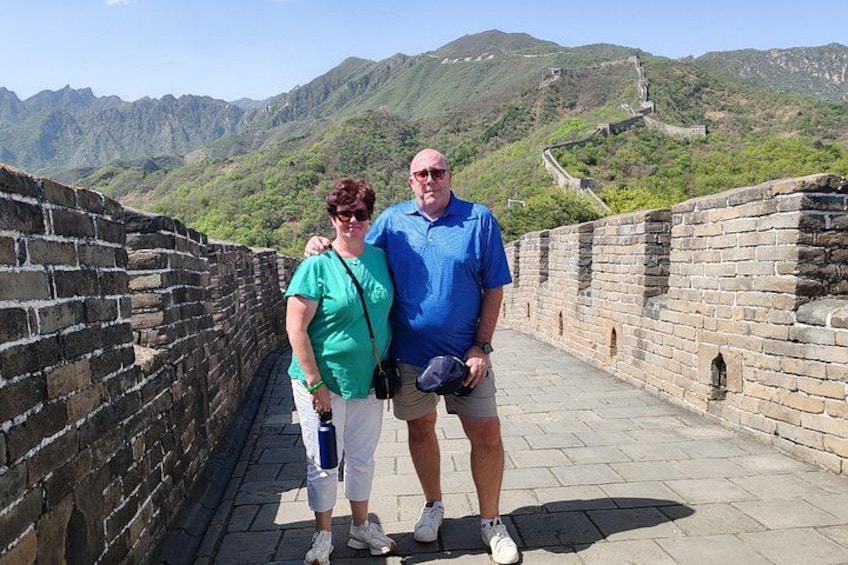 A man and a woman standing on a stone wall with a mountainous landscape in the background. 5