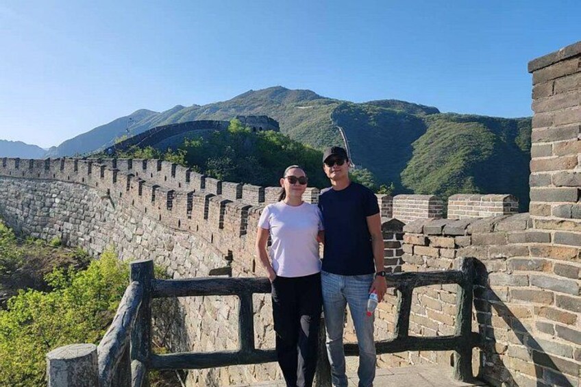Two people standing on the Great Wall of China with mountains in the background. 4