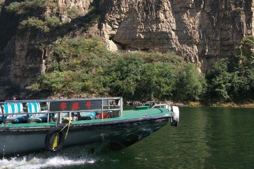 A boat with passengers, a rocky cliff, and greenery in the background. 5