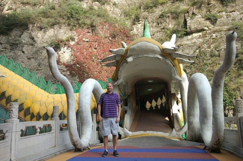 A man standing in front of a dragon-shaped tunnel entrance. 4