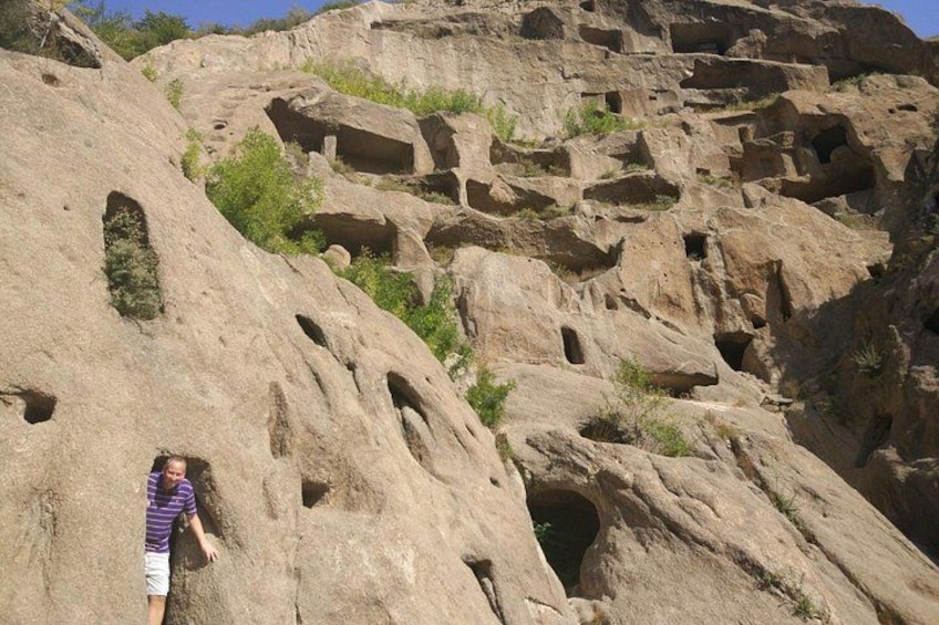 A person standing on a rocky cliff with multiple cave-like openings. 2