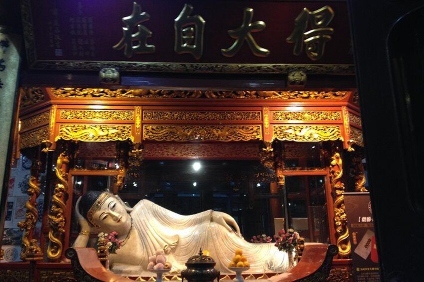 A statue of a reclining figure in a temple setting with ornate golden decorations and Chinese characters above. 3