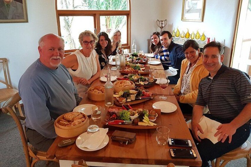 A group of people seated around a wooden table with various dishes and drinks. 4