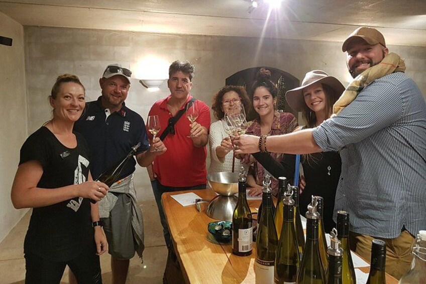 A group of people toasting with wine glasses around a table with bottles. 5