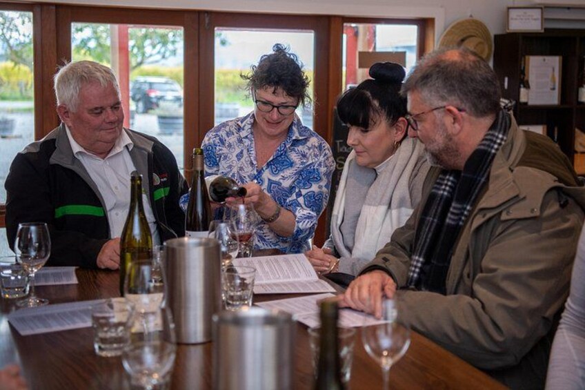 A group of people seated at a table with wine bottles and glasses. 1