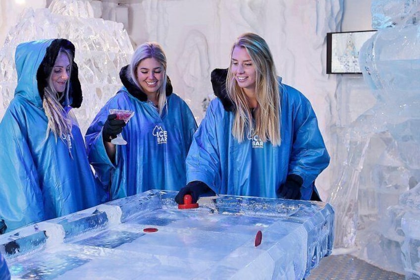 Tres personas con ponchos impermeables azules en un bar de hielo, con una gran escultura de hielo al fondo. 4