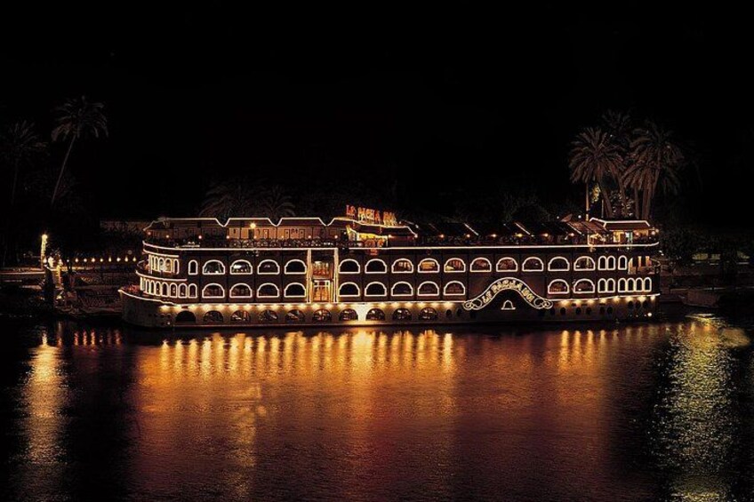 Un grand bateau illuminé, doté de plusieurs ponts et d’une passerelle, est amarré pendant la nuit. 4