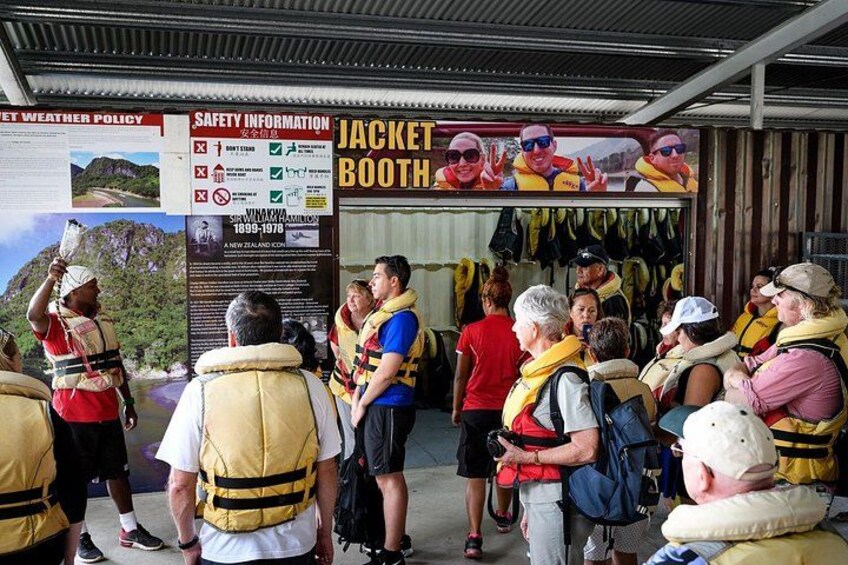 Un grupo de personas en un puesto de venta de chaquetas, algunas con chalecos salvavidas, con carteles de información de seguridad y un mapa al fondo. 2