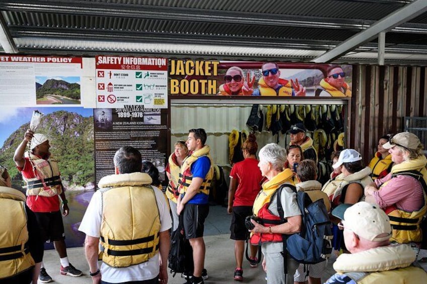 A group of people at a jacket booth, some wearing life jackets, with safety information signs and a map in the background. 2