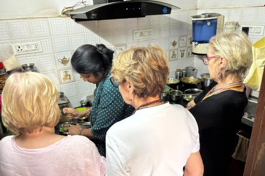 Un grupo de personas en una cocina con paredes de azulejos blancos, una estufa y diversos utensilios de cocina. 2