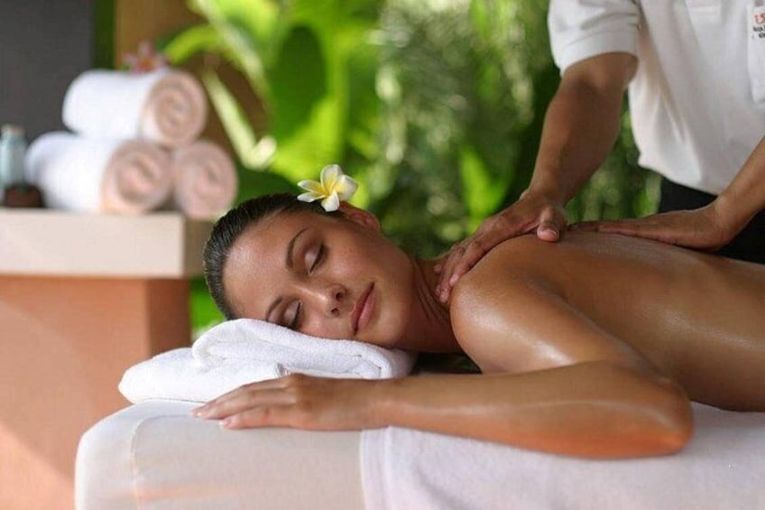 A person receiving a massage in a spa setting with towels and greenery in the background. 1