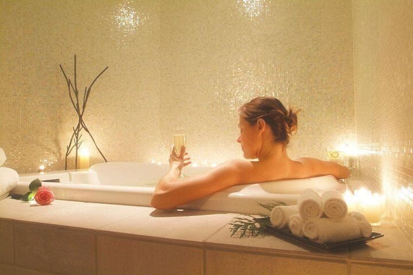 A person relaxing in a bathtub with towels and a glass of water. 3