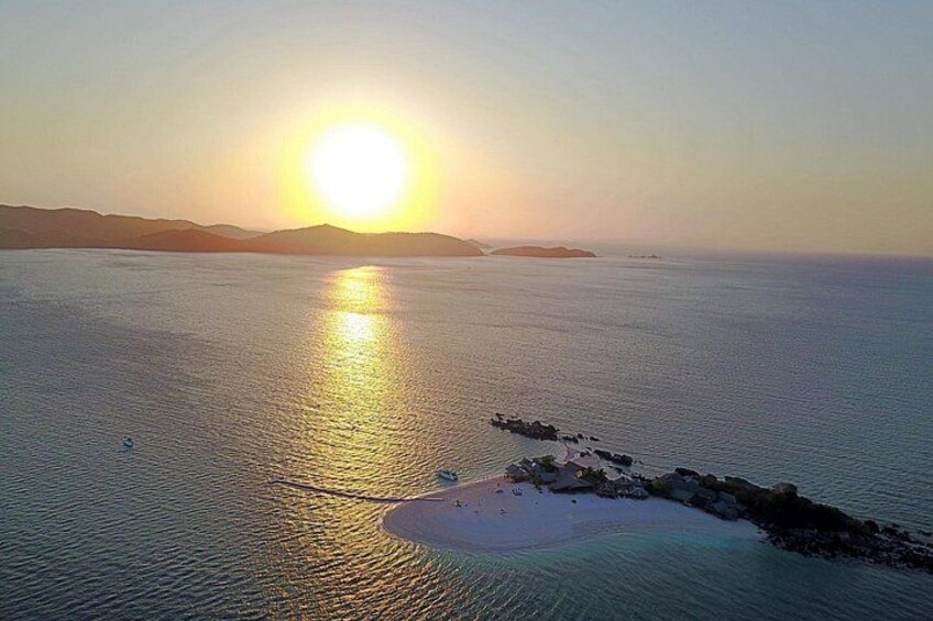 A sunset over a calm sea with a small island and distant landforms. 1