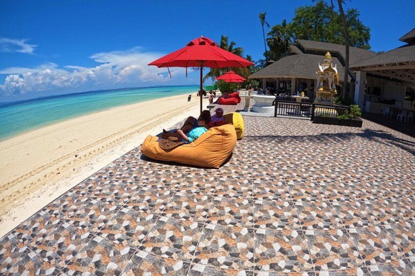 Ein Strand mit einem gefliesten Weg, einer goldenen Statue und roten Sonnenschirmen. 3
