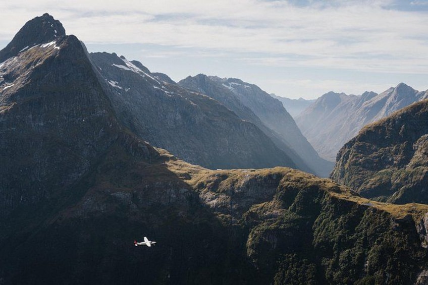 Un paisaje montañoso con un valle y un avión volando sobre él. 3