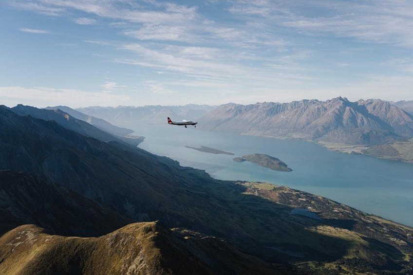 Un avión volando sobre un paisaje montañoso con un lago. 5