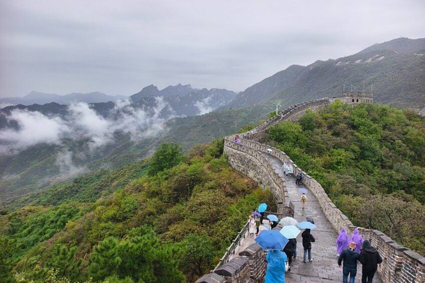 A stone pathway with people walking, surrounded by lush greenery and mountains. 2