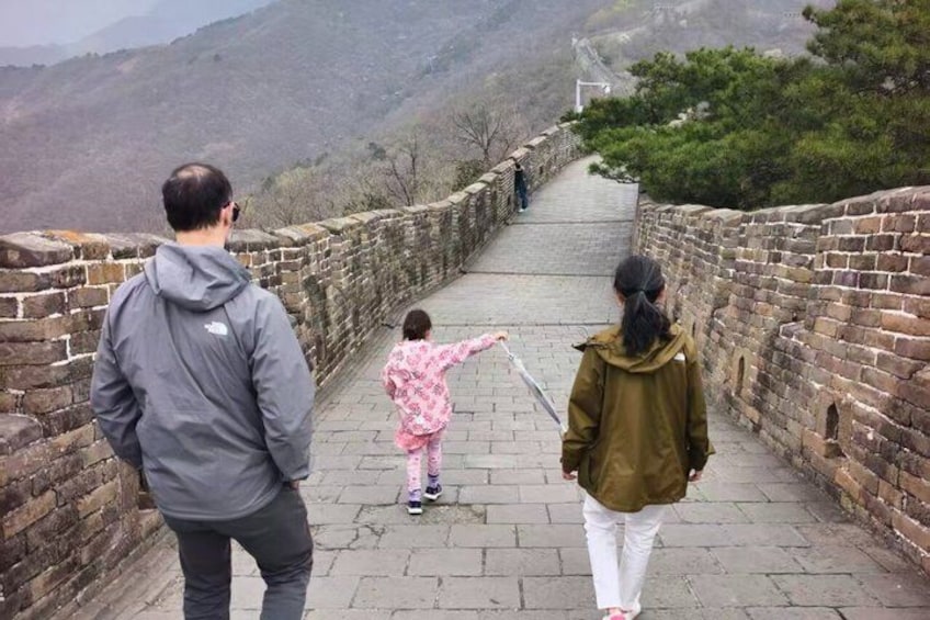 A person in a green jacket and white pants walking on the Great Wall of China. 4