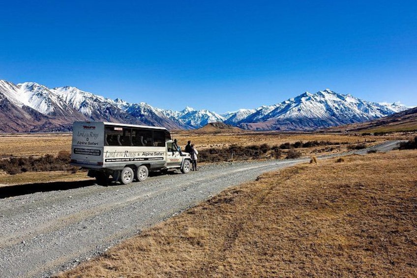 Un autobús turístico en un camino de grava con montañas nevadas al fondo. 2