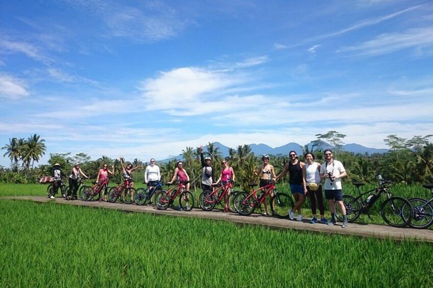 A group of people on bicycles in a rural setting with green fields and mountains in the background. 2