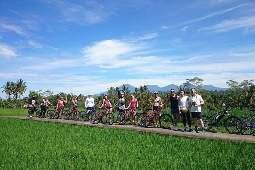 A group of people on bicycles in a rural setting with green fields and mountains in the background. 2