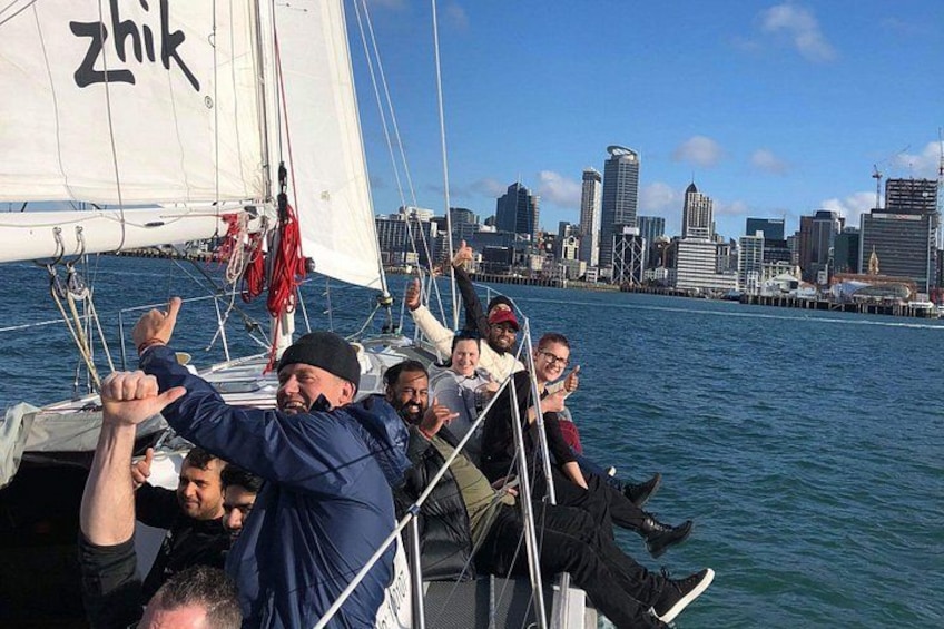 A sailboat with people on board, a city skyline in the background, and a body of water. 3