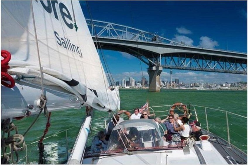 A sailboat with people on board, a bridge in the background, and a city skyline. 2