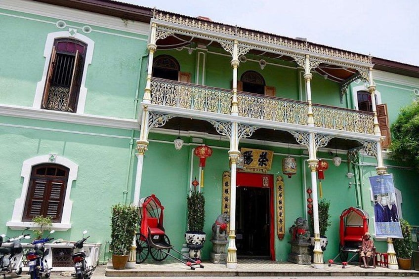A green building with ornate balconies, a red door, and traditional decorations. 1