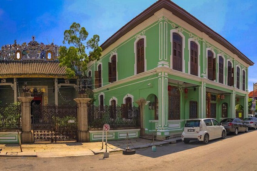 A green colonial-style building with a tiled roof, a gated entrance, and parked cars. 2