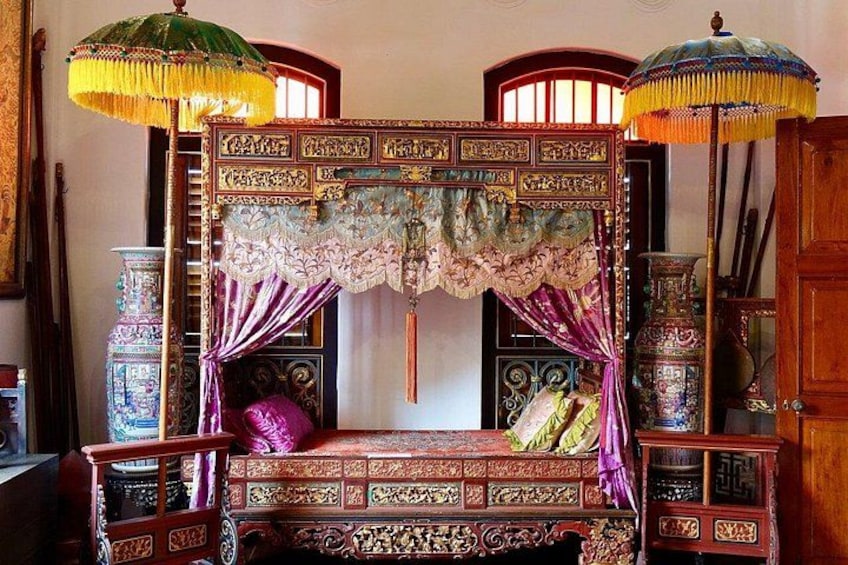 An ornate bed with intricate carvings, a canopy with tassels, and traditional furniture. 3