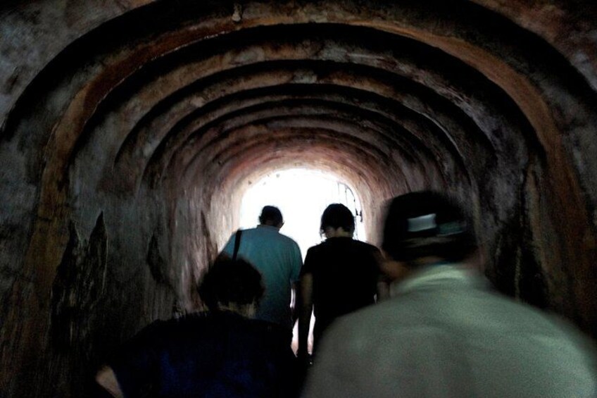 A tunnel with arched ceilings and a person walking towards the light at the end. 2
