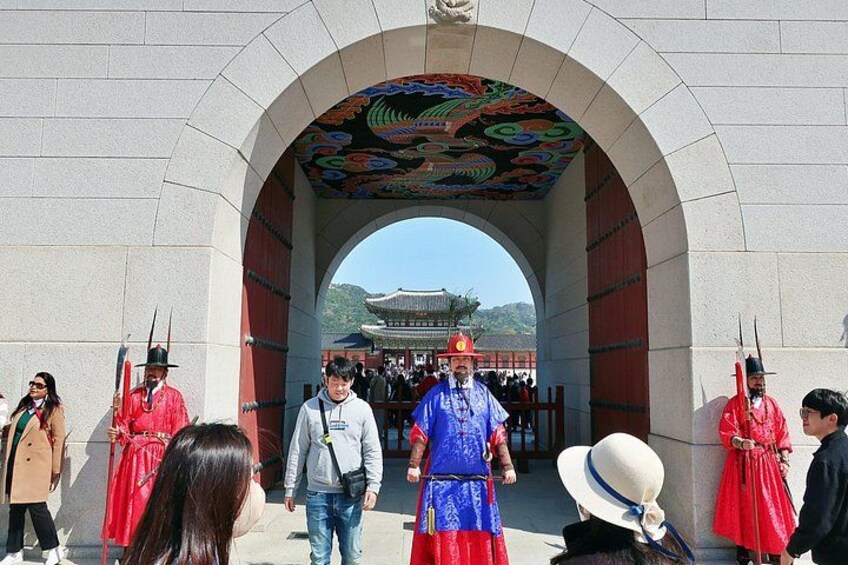 A traditional Korean gate with a colorful roof, people in traditional attire, and a modern building in the background. 2